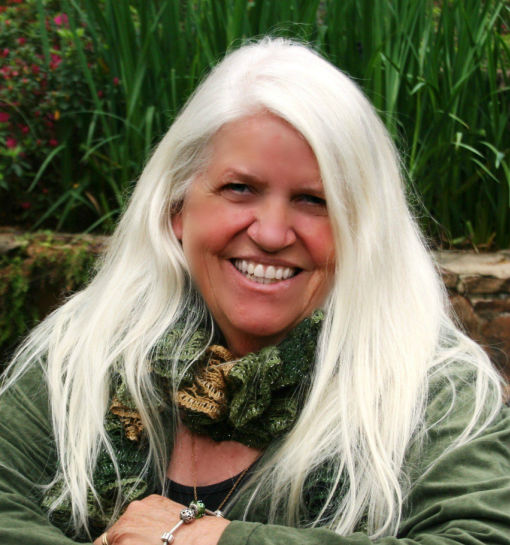 Caryl McAdoo in green sitting near a brick wall at a park.